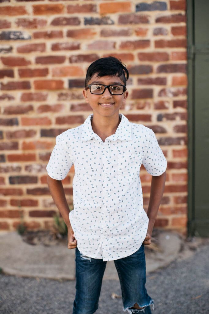 boy in white shirt and blue jeans with glasses smiling